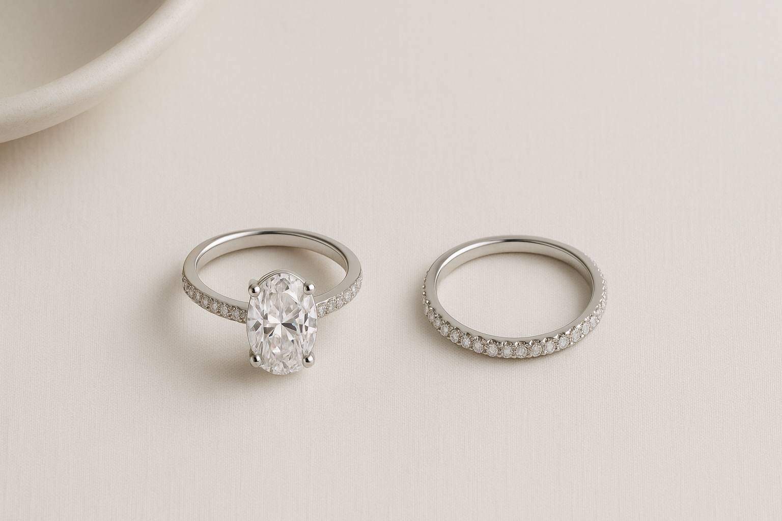 Two silver rings a solitaire-style dupe and a slim pavé eternity band centered on neutral linen, illustrating how to test engagement ring styles with travel ring dupes.