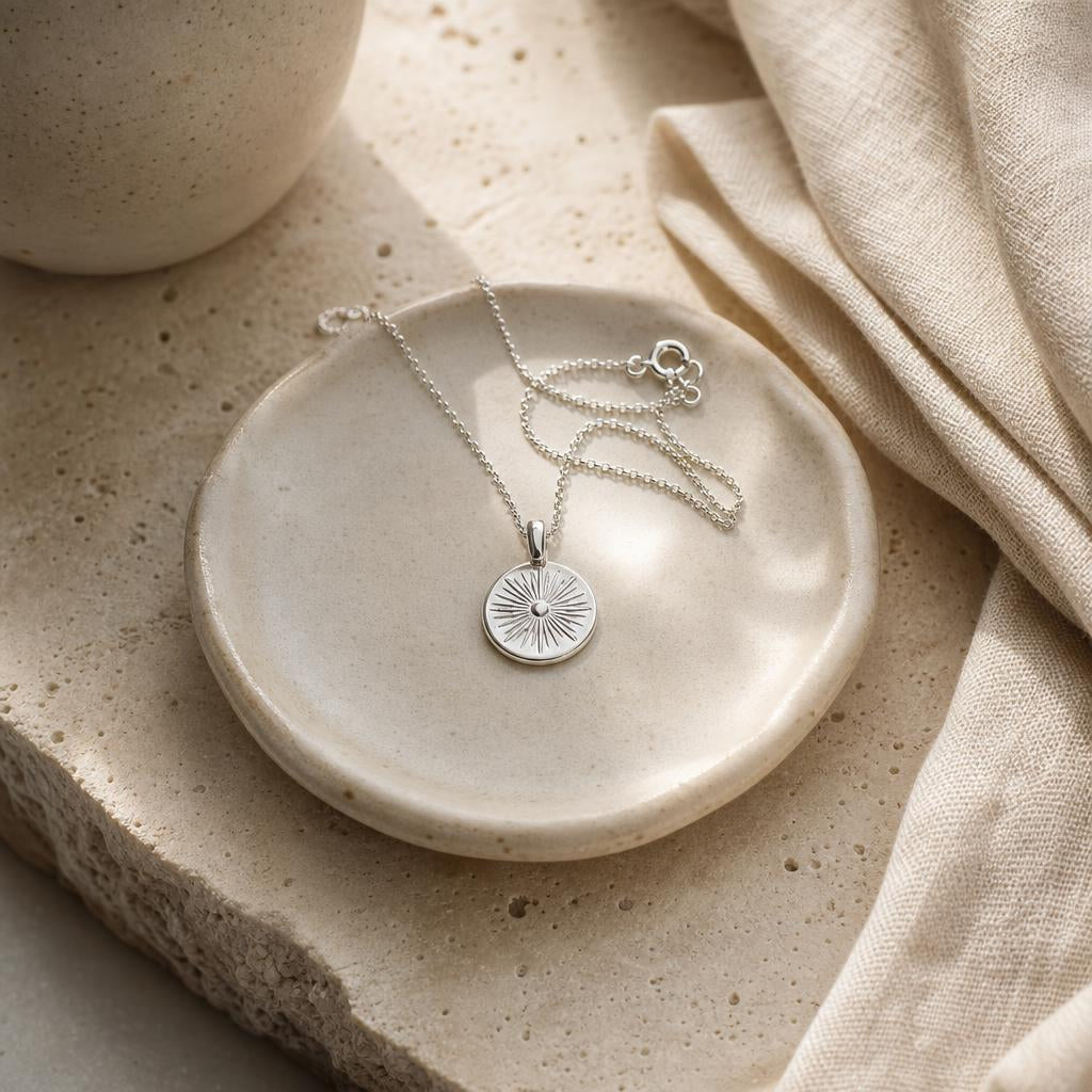 Silver pendant necklace resting on a ceramic dish beside cream linen