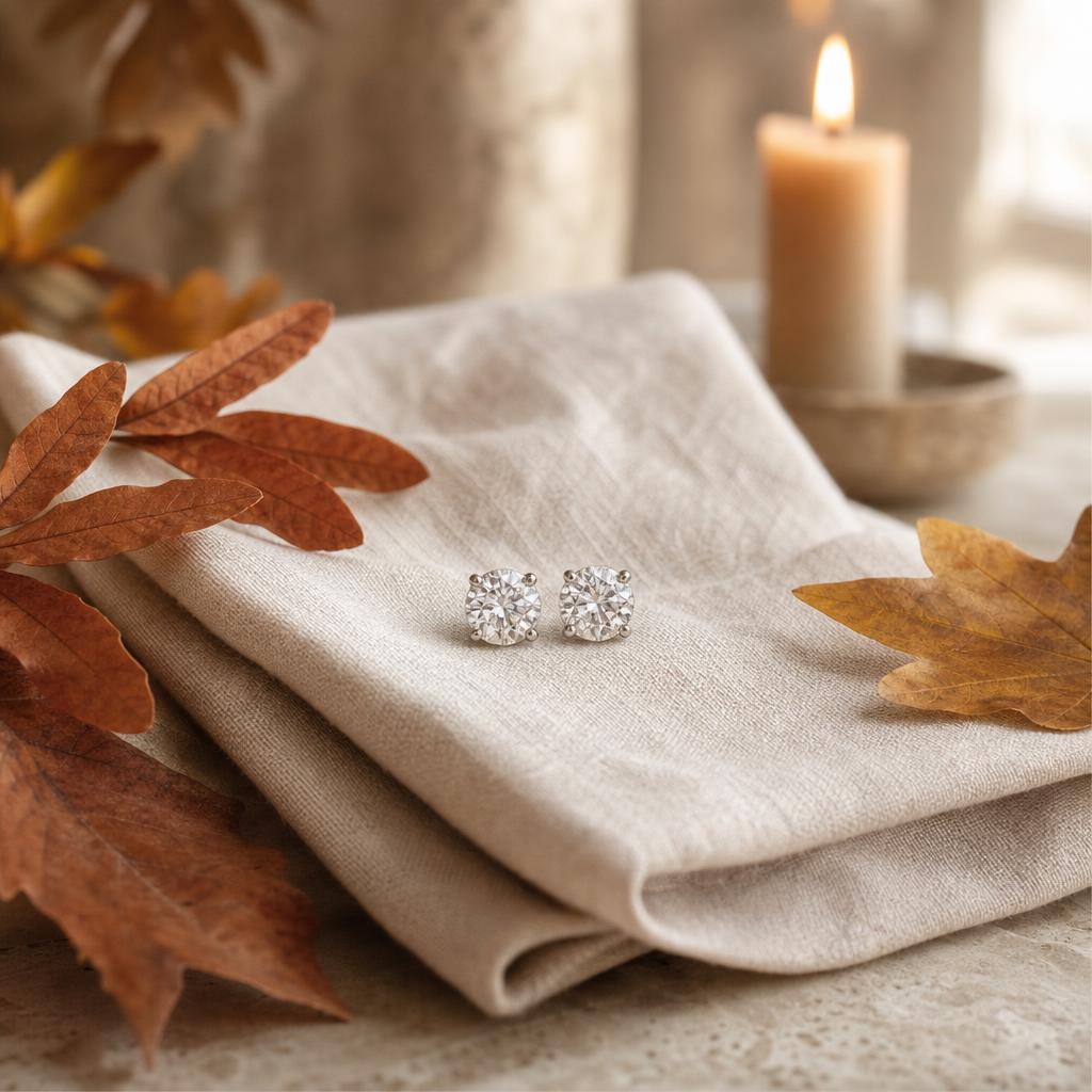 Pair of sparkling stud earrings on cream linen with autumn leaves