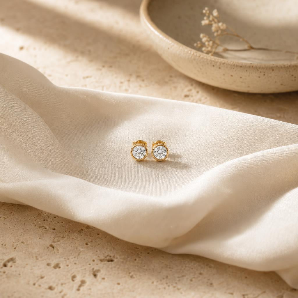 Pair of small stud earrings resting on cream silk beside a jewelry dish