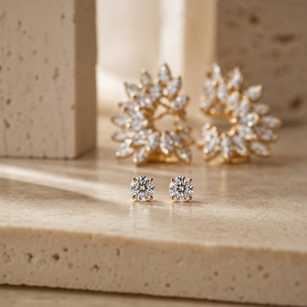 Small sparkling round stud earrings on a warm cream stone surface
