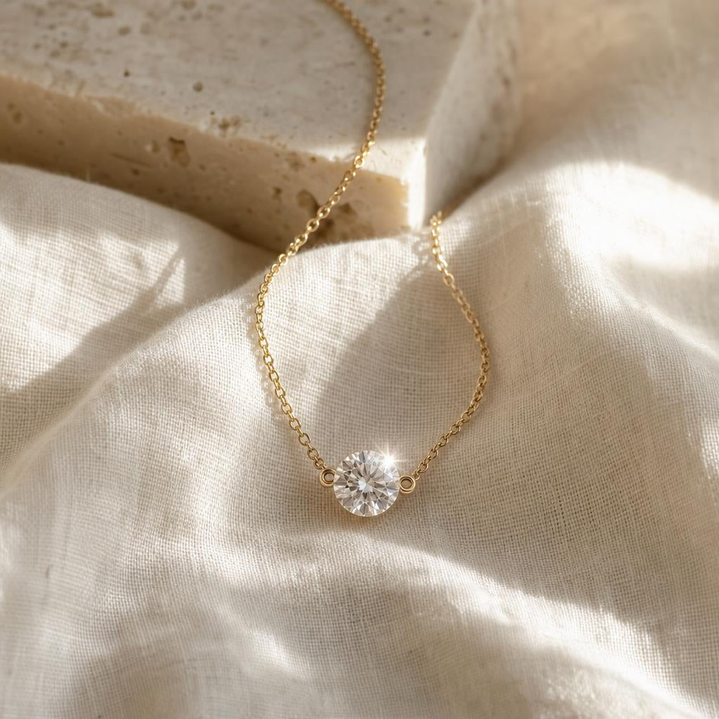 Round solitaire pendant on fine chain resting on cream linen in soft light