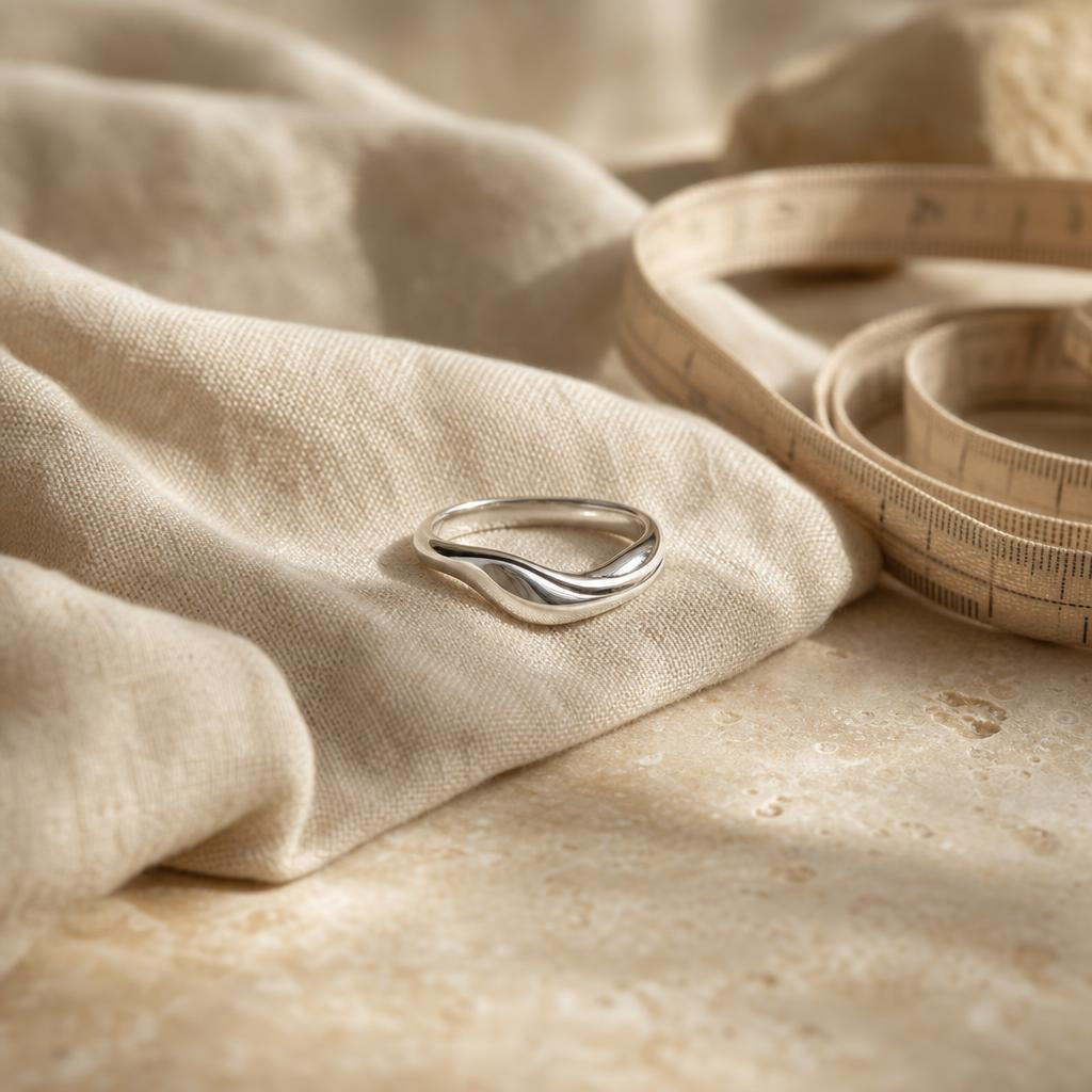 Sterling silver ring resting on cream linen beside a coiled measuring tape