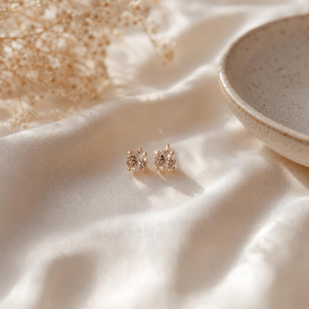 Delicate minimalist stud earrings resting on soft cream silk fabric
