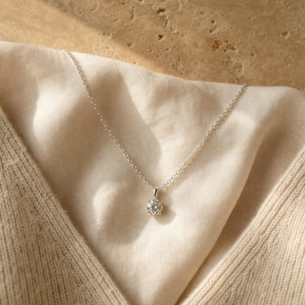 Silver pendant necklace draped in a V shape on cream linen