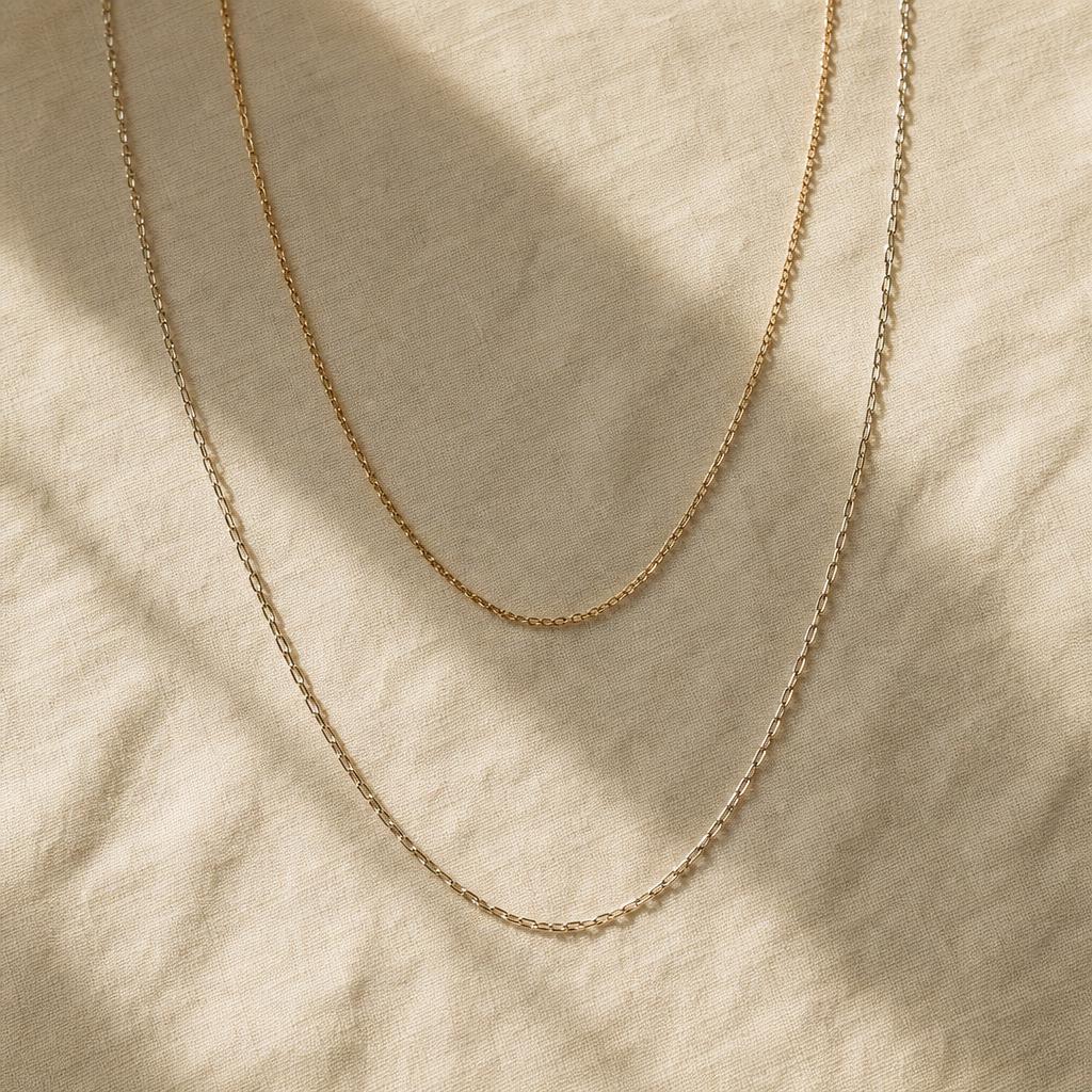 Three delicate necklace chains of varying lengths draped on cream linen