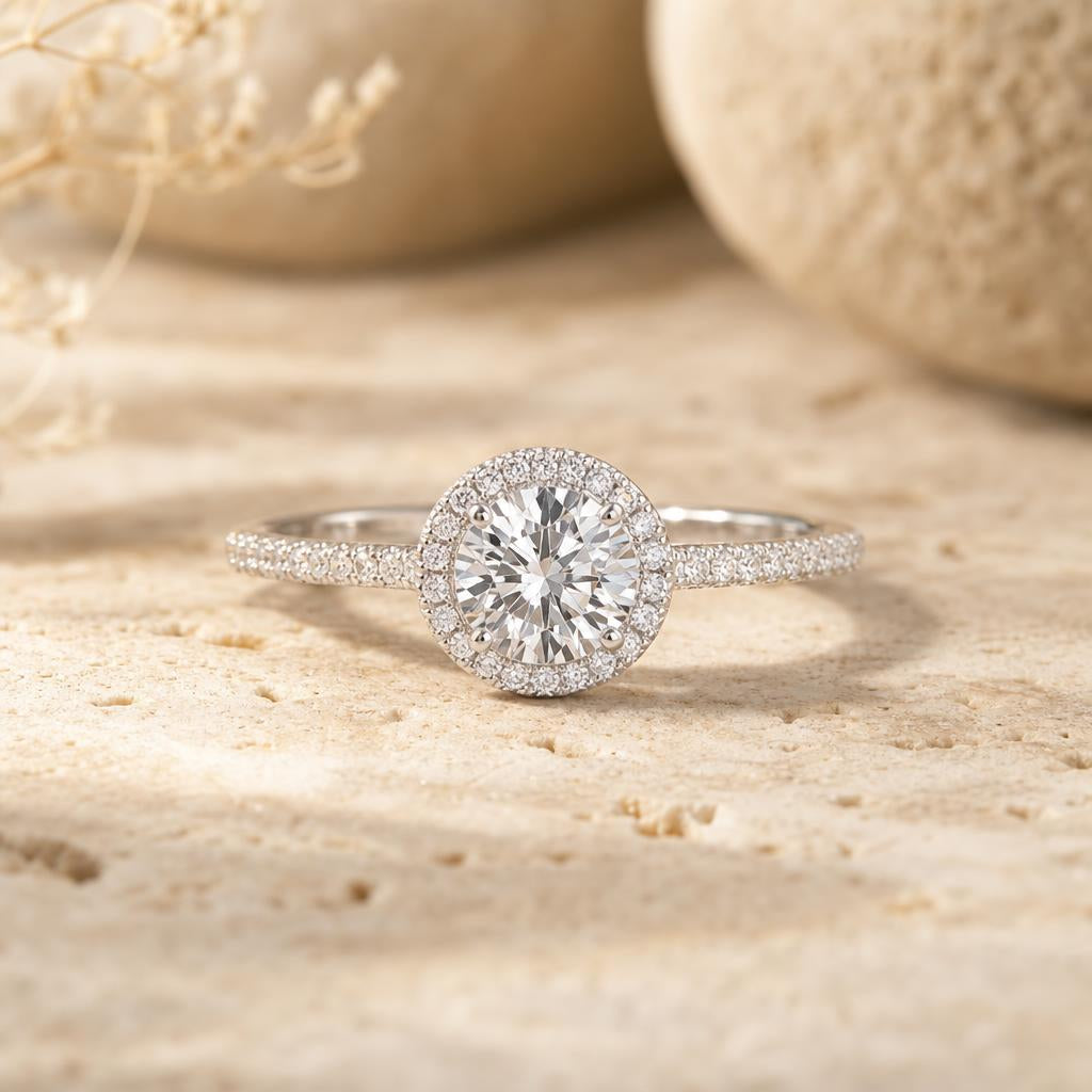 Round brilliant simulated diamond ring with pavé band and halo resting on warm cream stone surface