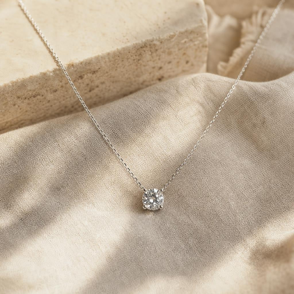 Single solitaire pendant necklace on a silver chain resting on cream linen