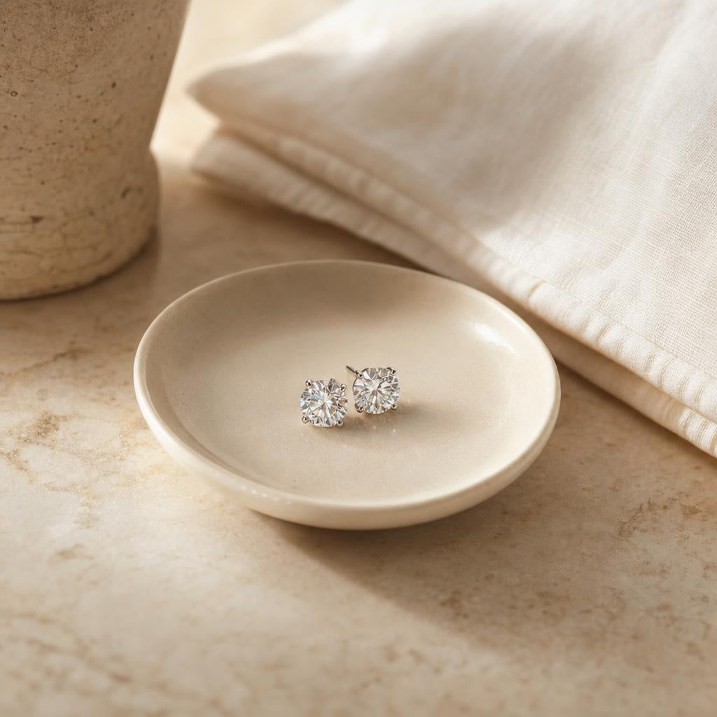 Pair of sparkling stud earrings in a cream dish beside a linen pillowcase