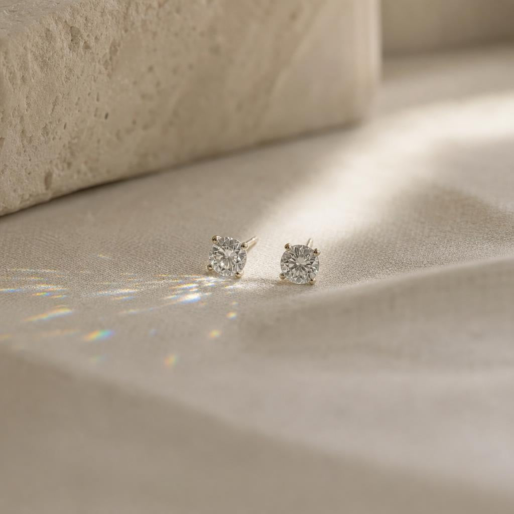 Pair of small round stud earrings catching soft window light on cream linen