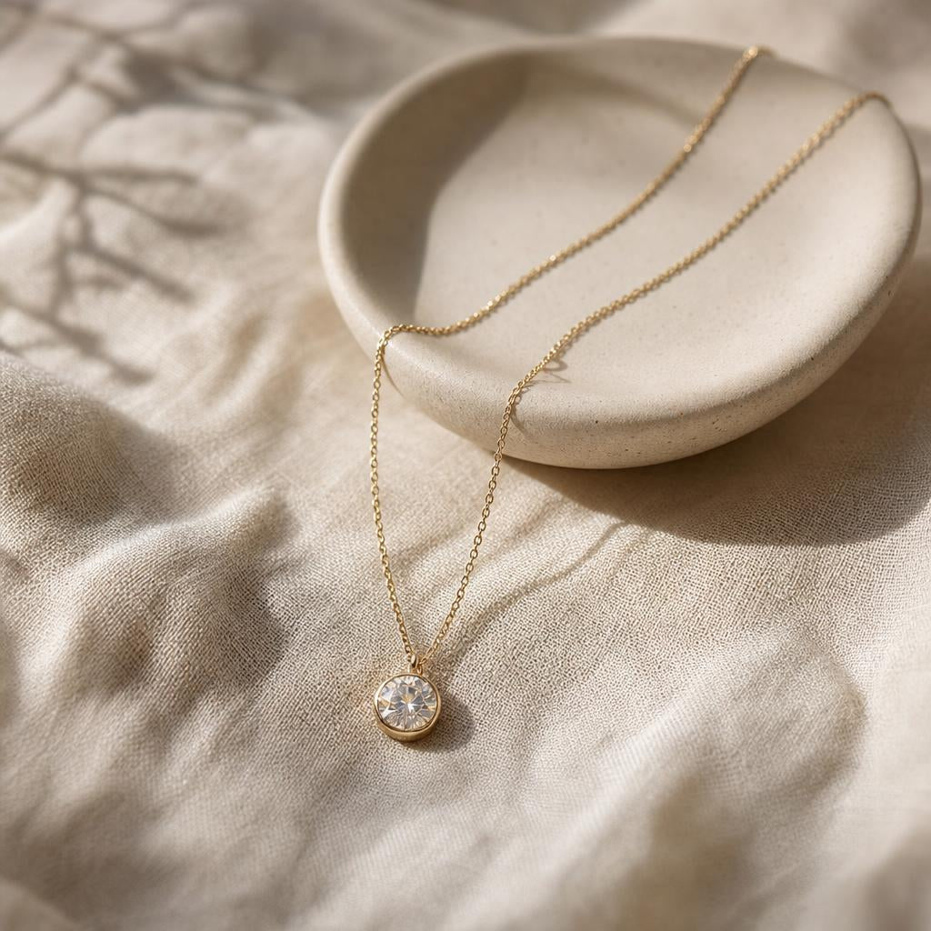 Fine round-stone pendant necklace resting on cream linen beside a ceramic dish