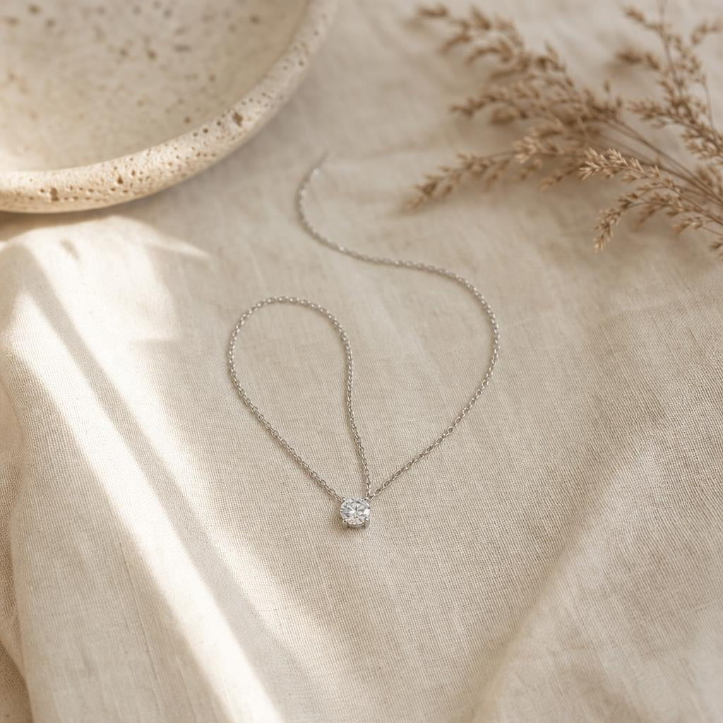 Fine silver pendant necklace curved on cream linen in soft morning light