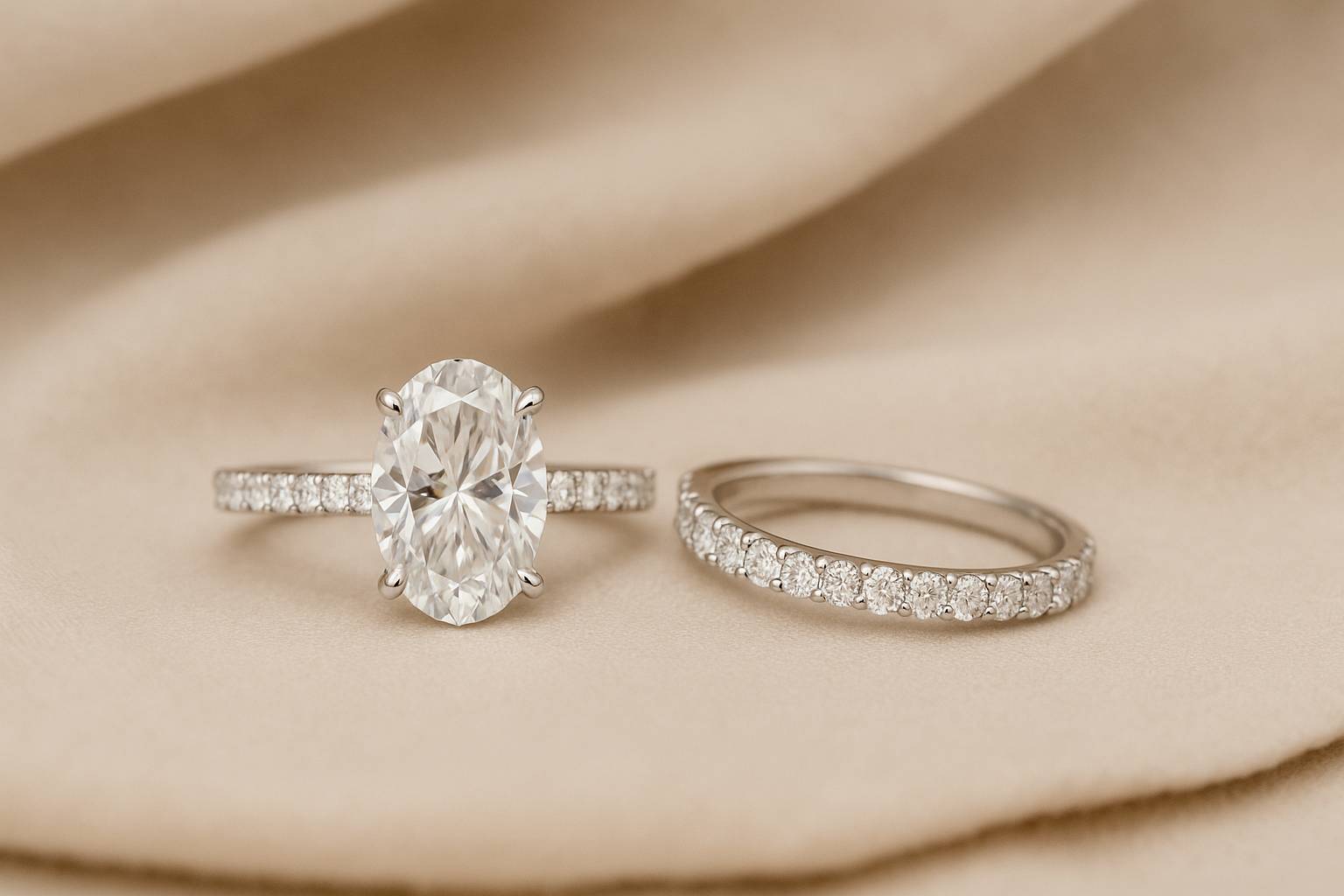 White gold oval solitaire engagement ring with two matching wedding bands displayed on a neutral jewelry pouch, showcasing pairing options for oval rings.