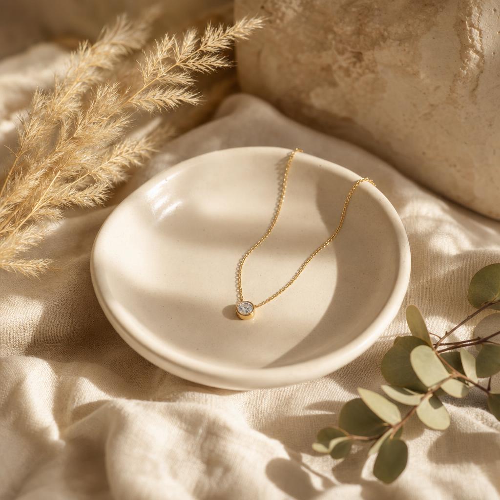 Delicate pendant necklace resting on a ceramic dish with soft warm light