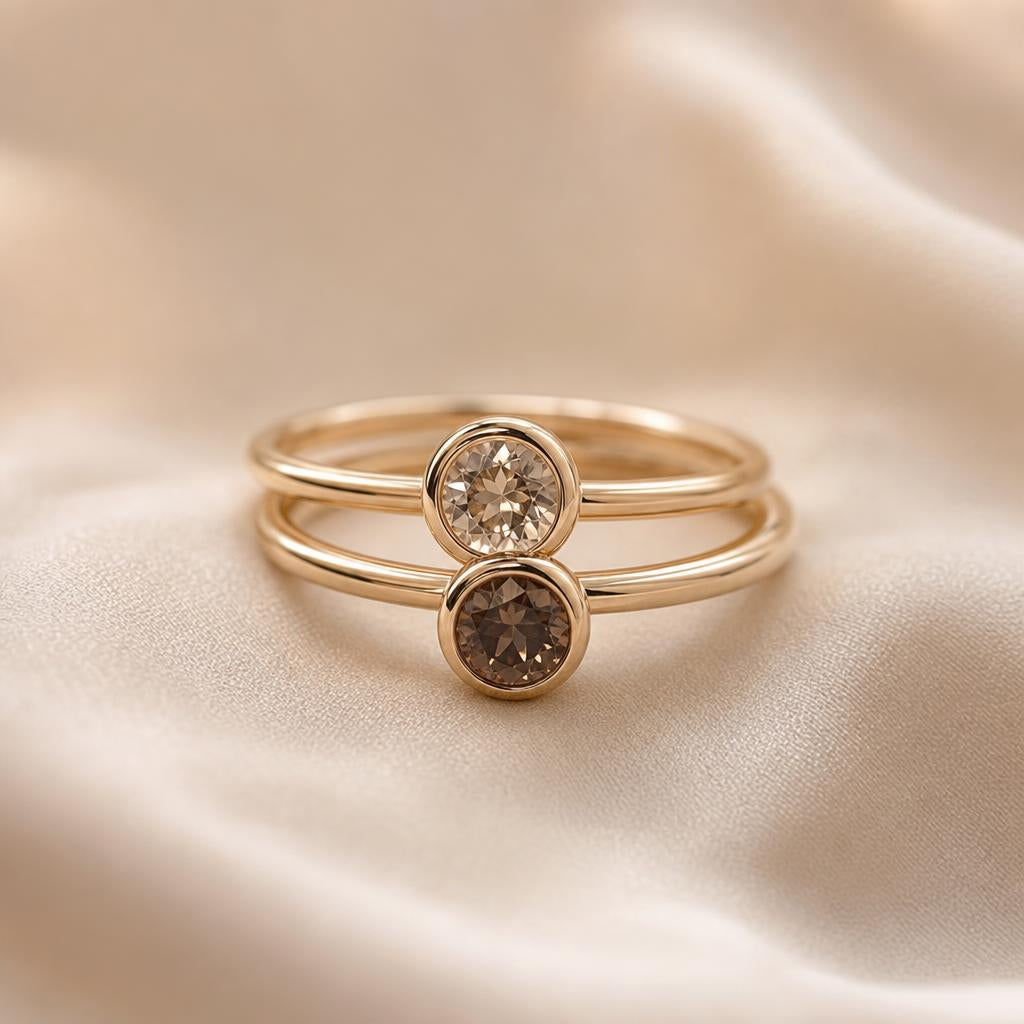 Two smooth bezel-set rings stacked together on a soft cream backdrop