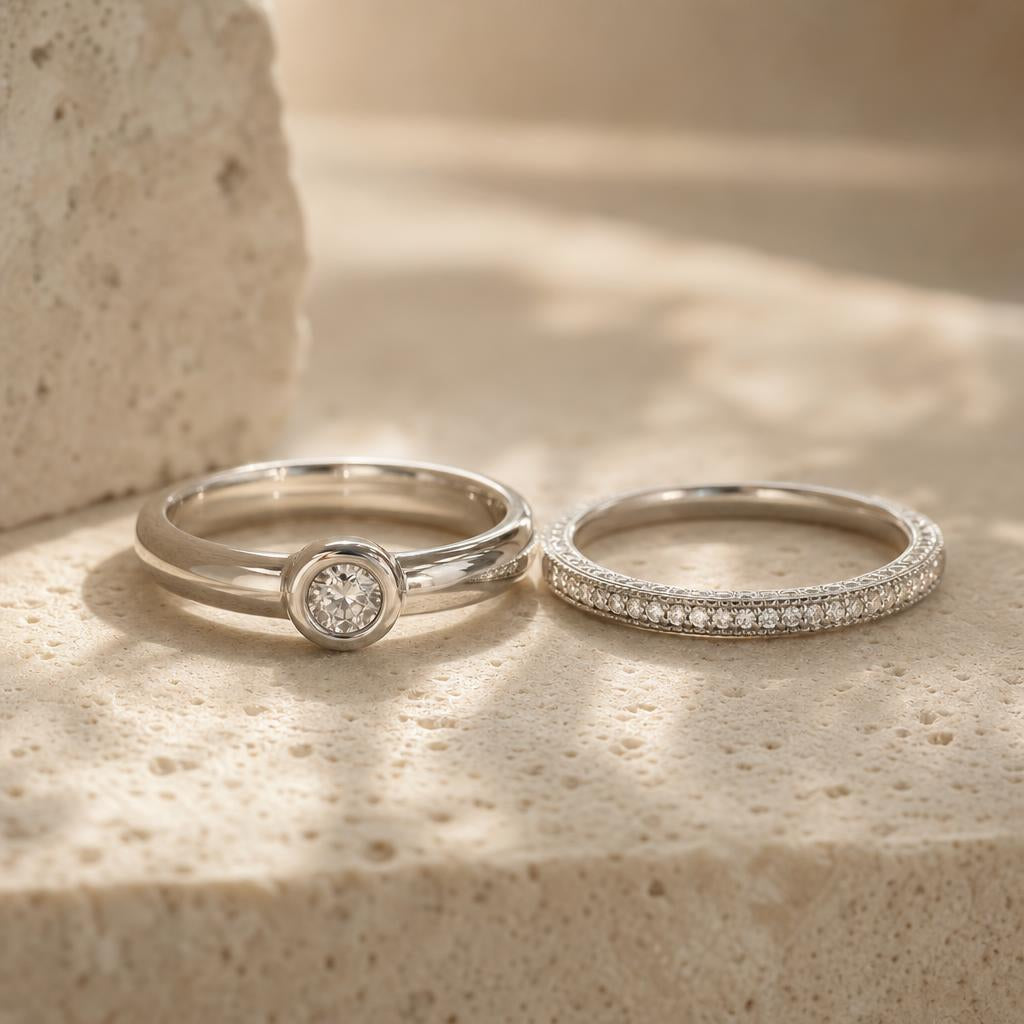 Two bezel-set and pavé silver stacking rings on a warm stone backdrop