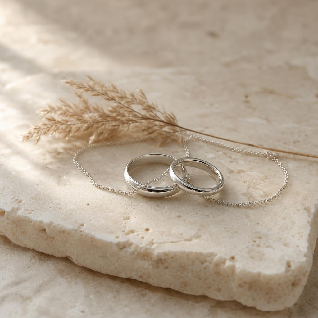 Two silver rings and a fine chain resting together on cream stone