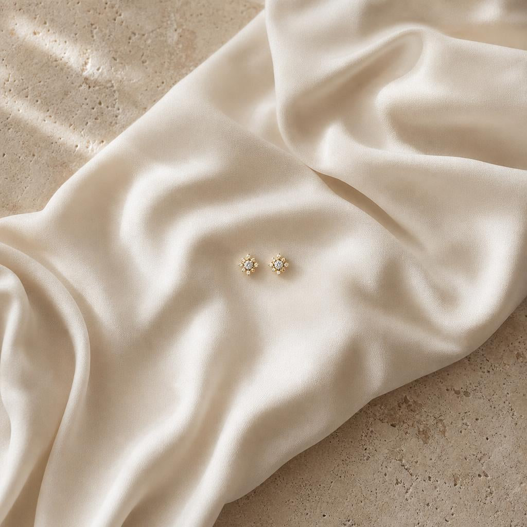 Delicate stud earrings centered on draped cream silk fabric, editorial still life