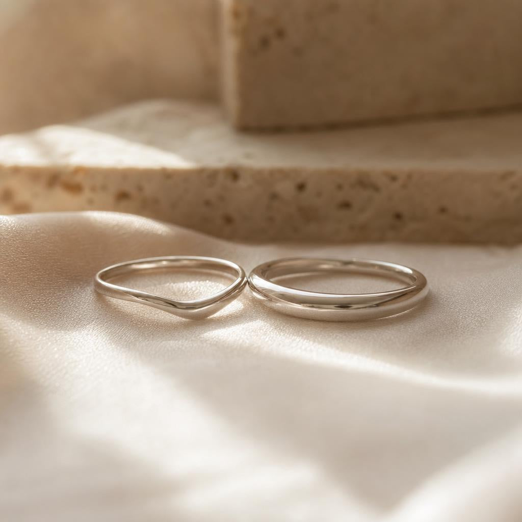 Two curved sterling silver rings nested together on warm cream silk fabric