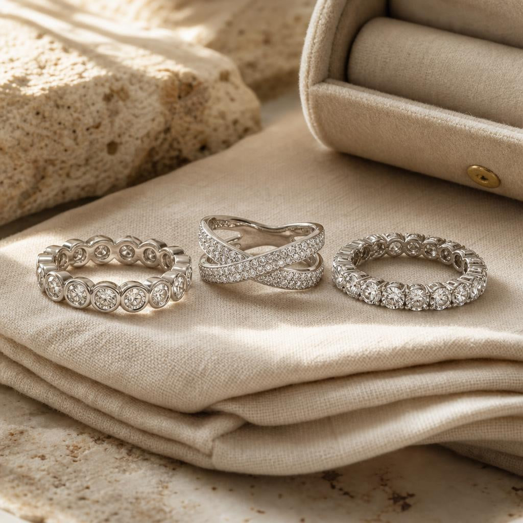 Three simulated diamond rings on cream linen cloth beside a velvet jewellery roll