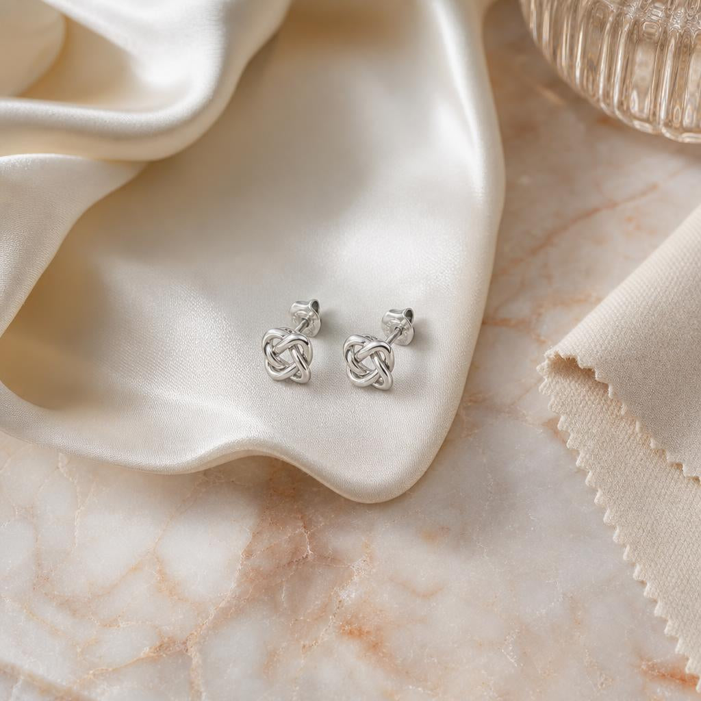 Pair of silver stud earrings resting on soft ivory fabric with polishing cloth