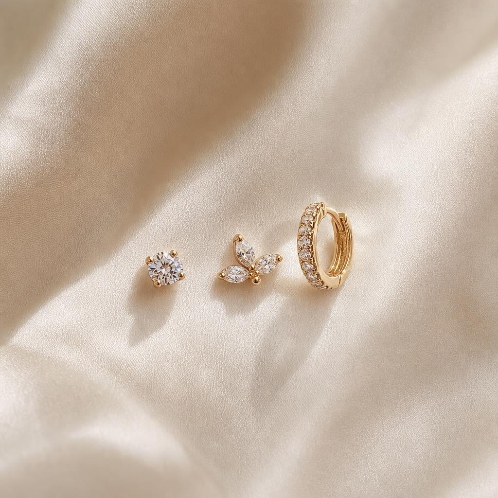 Delicate stud and hoop earrings arranged in an ascending stack on cream silk