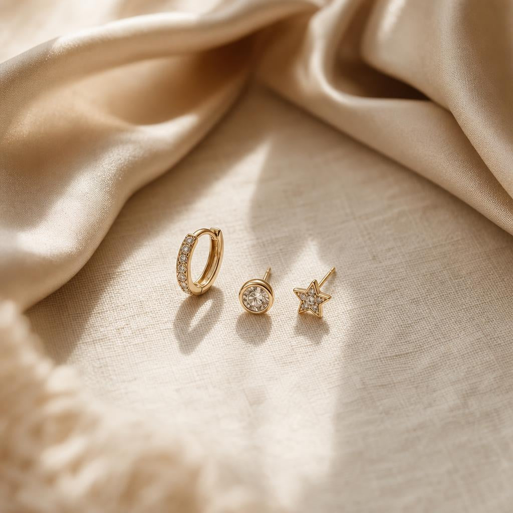 Three small stacked earrings arranged on soft cream linen fabric