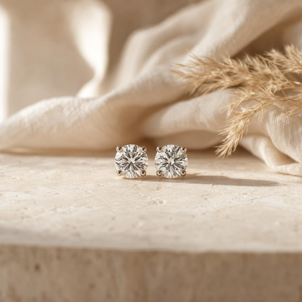 Pair of sparkling round stud earrings on a warm cream stone surface