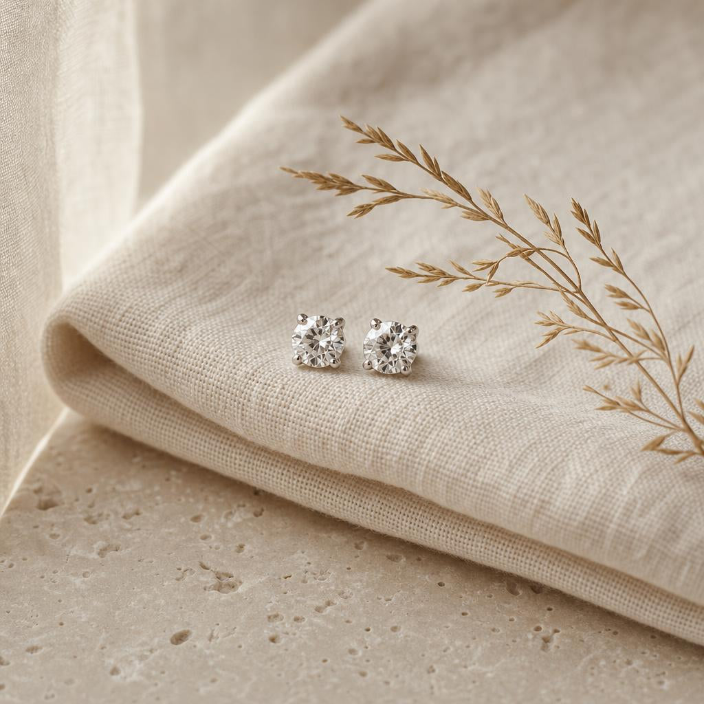 Pair of sparkling stud earrings on warm cream linen with dried grass