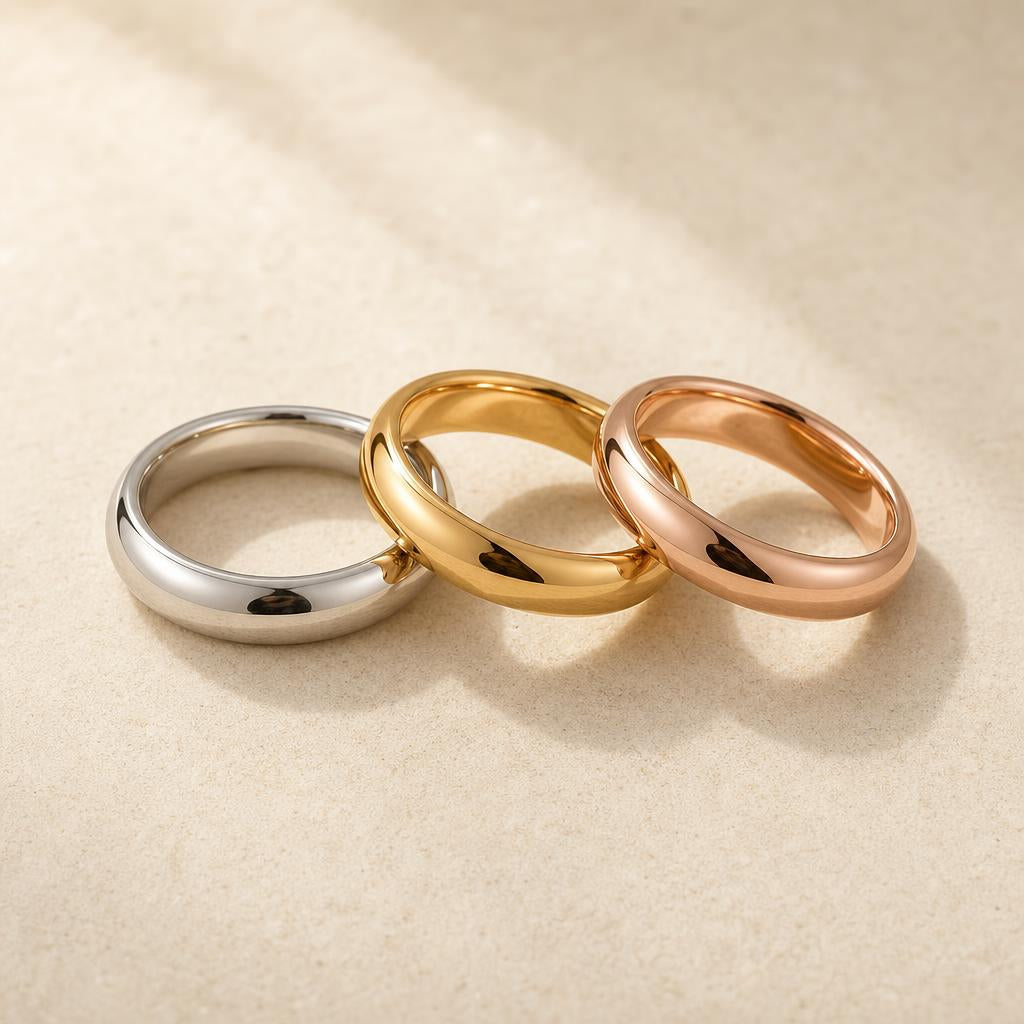 Three ring bands in rhodium white, yellow gold, and rose gold on cream stone surface