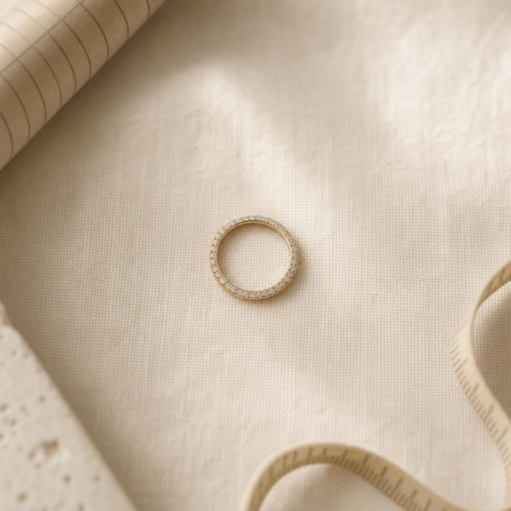 Delicate pavé ring resting on cream linen beside a sizing mandrel