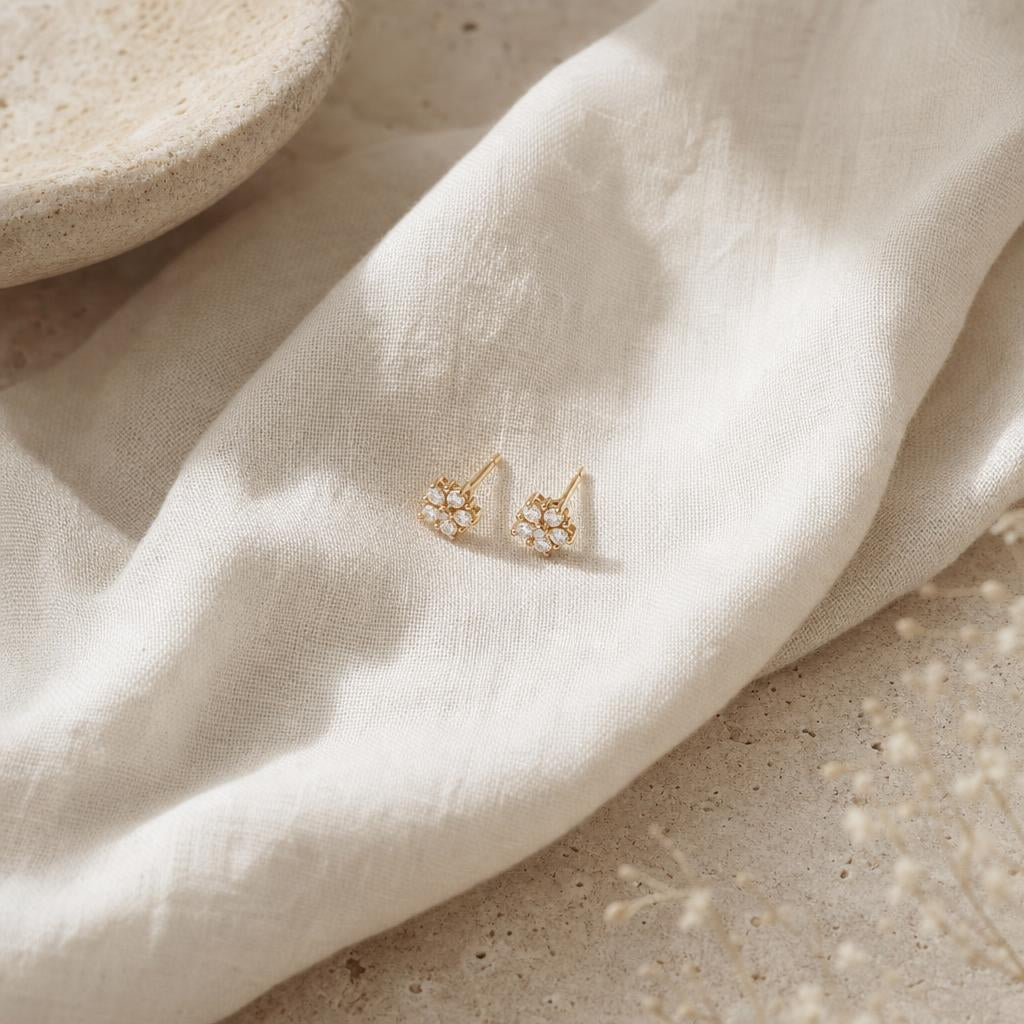 Delicate stud earrings resting on folded ivory linen against a cream background