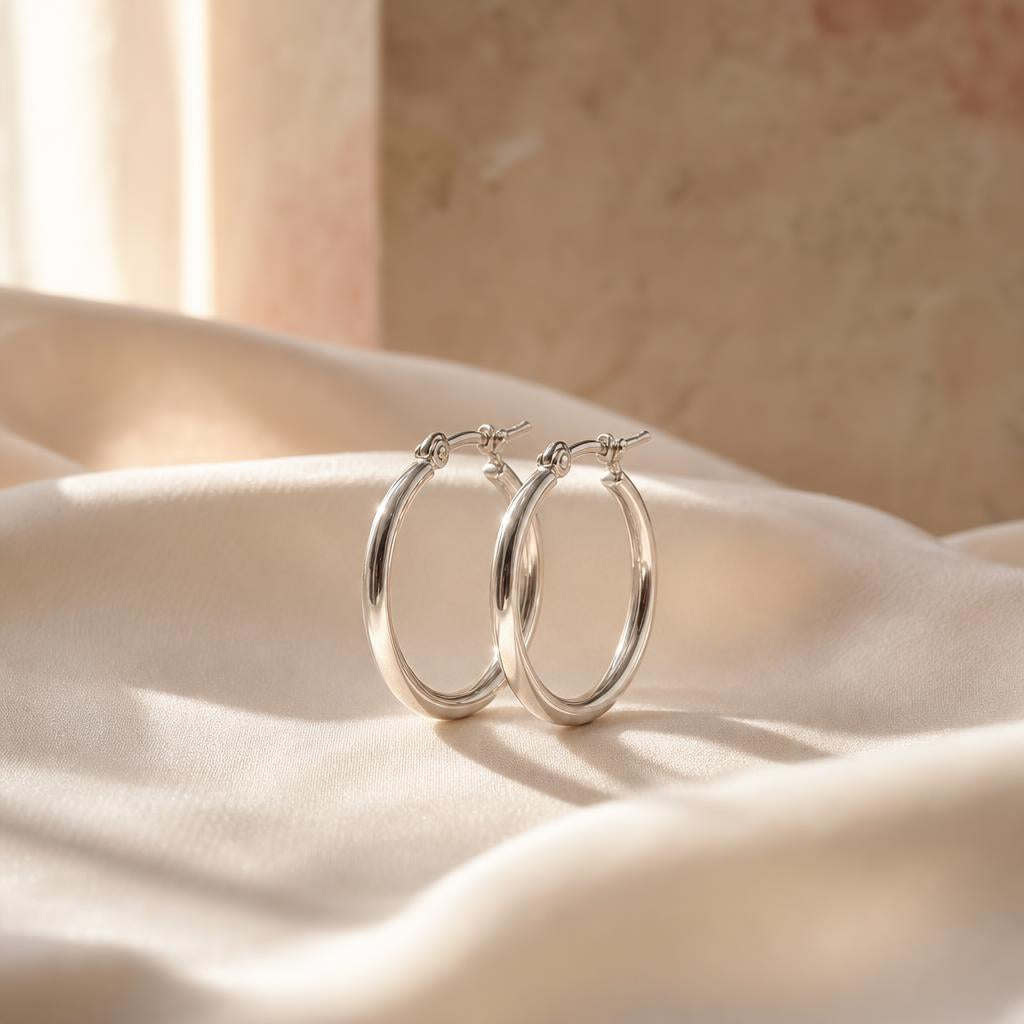 Warm silver hoop earrings resting on soft cream silk fabric