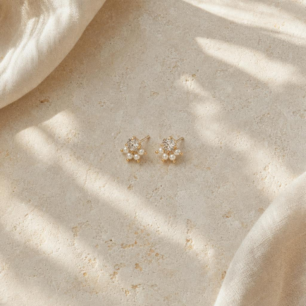Warm editorial close-up of stud earrings on cream stone background