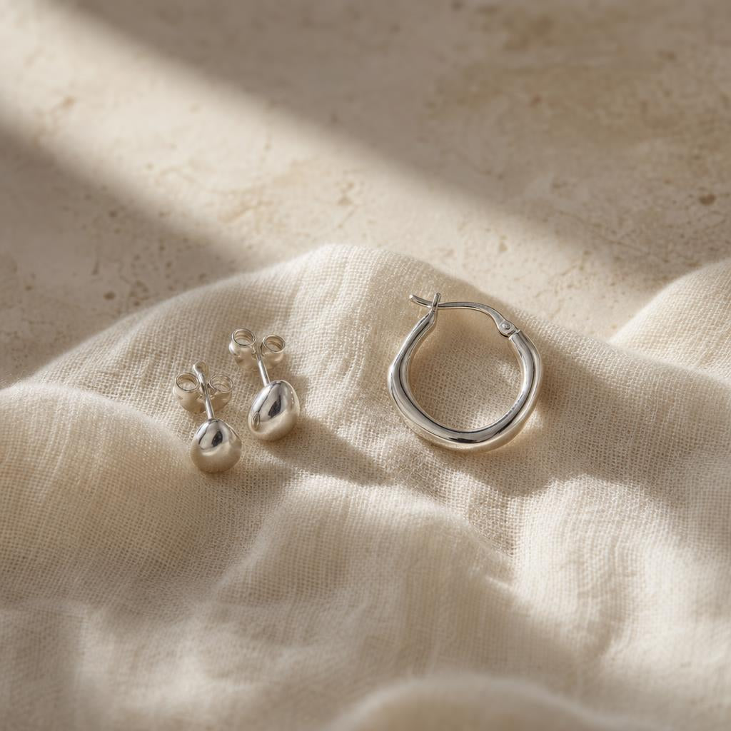 Delicate silver stud and hoop earrings on soft ivory linen fabric