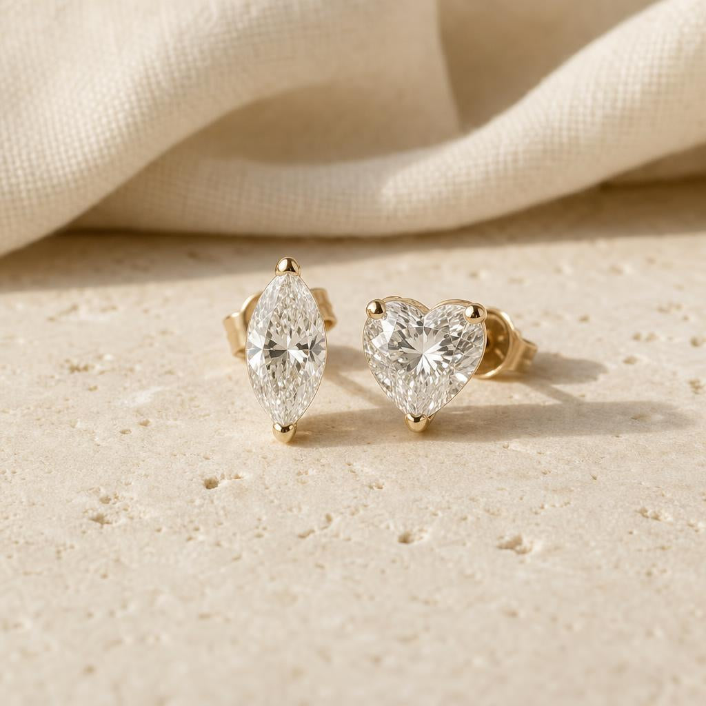 Marquise and heart-shaped sparkling stud earrings on a warm cream stone surface