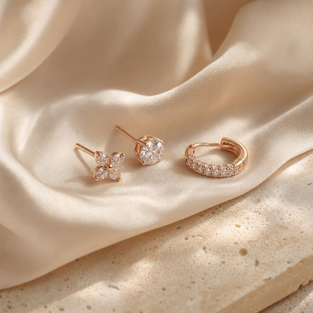 Delicate minimalist stud and huggie hoop earrings on warm cream fabric