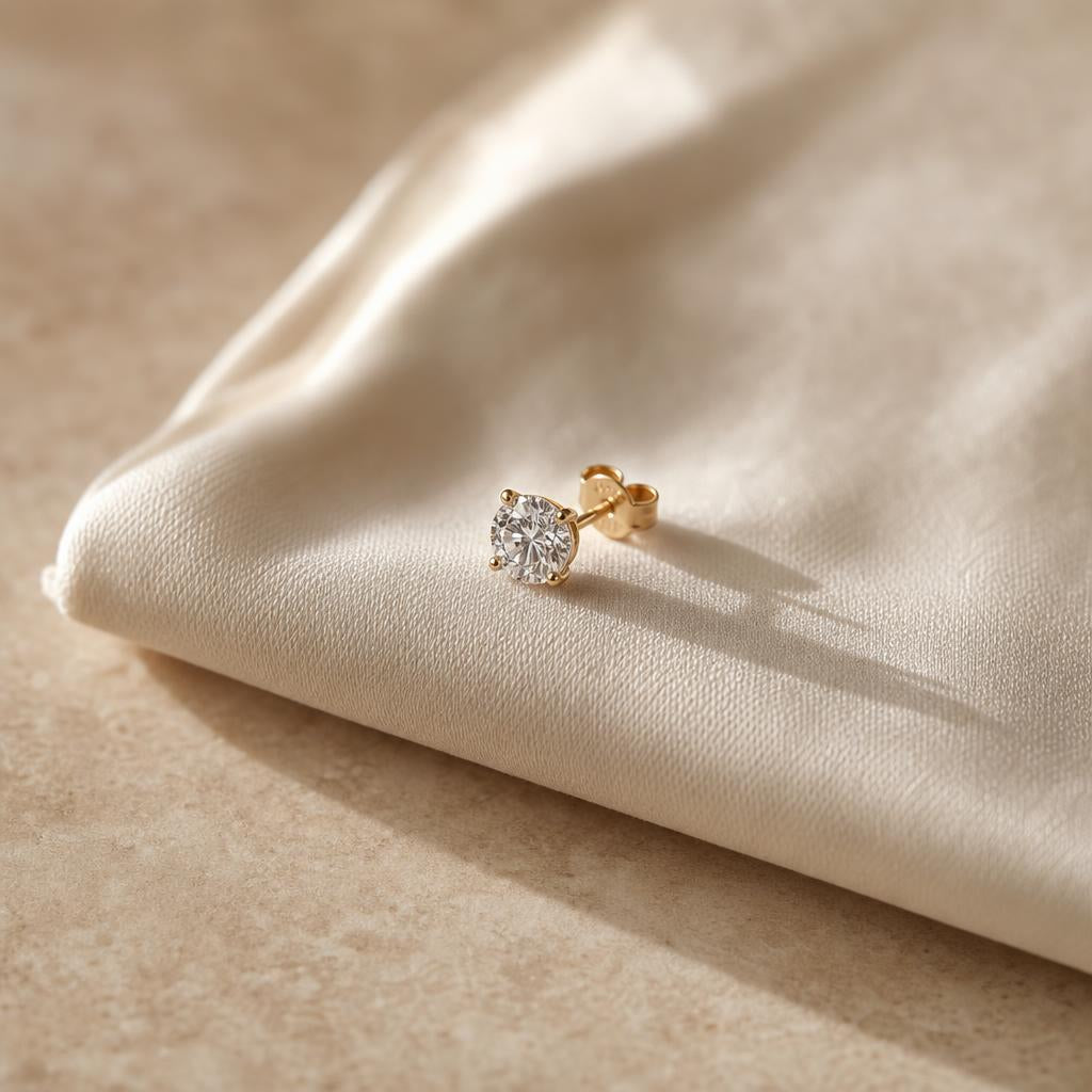 Single sparkling stud earring resting on soft cream silk fabric