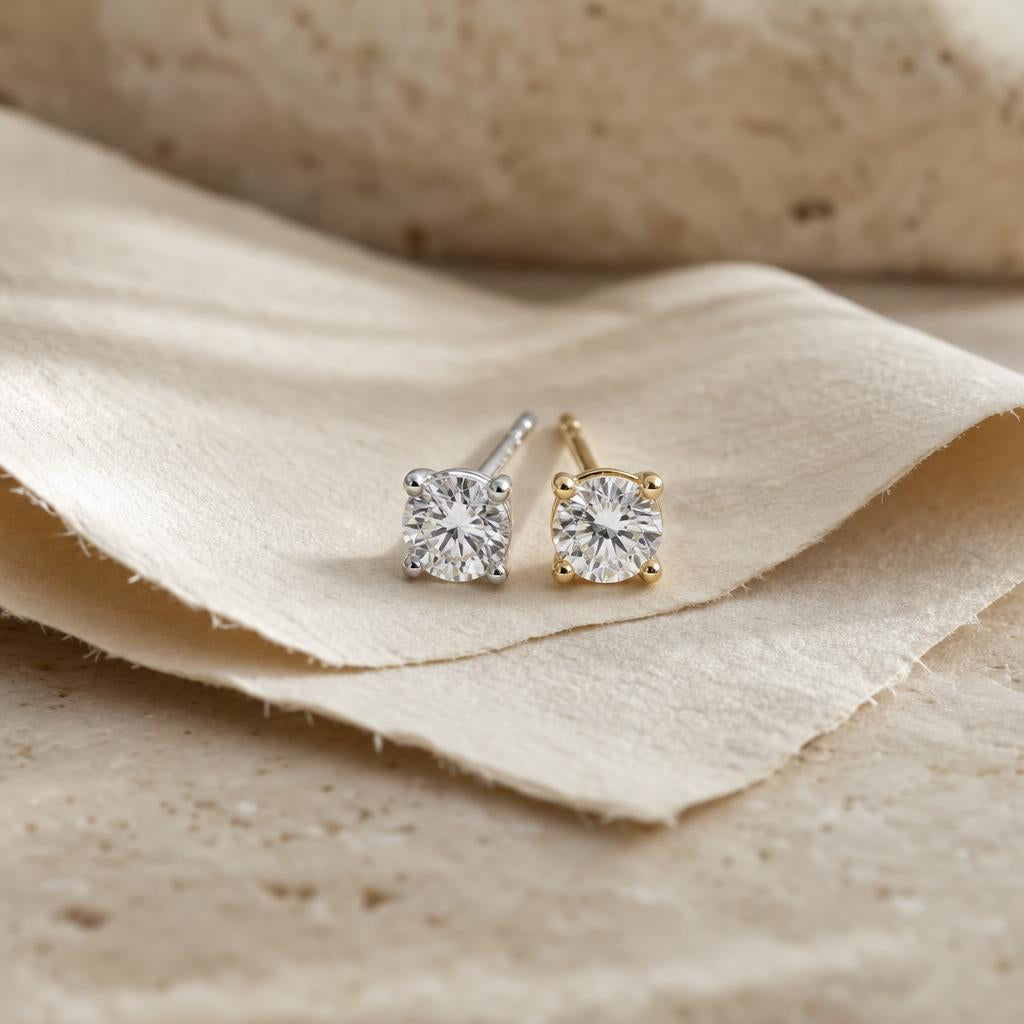 Silver and gold stud earrings resting side by side on cream linen