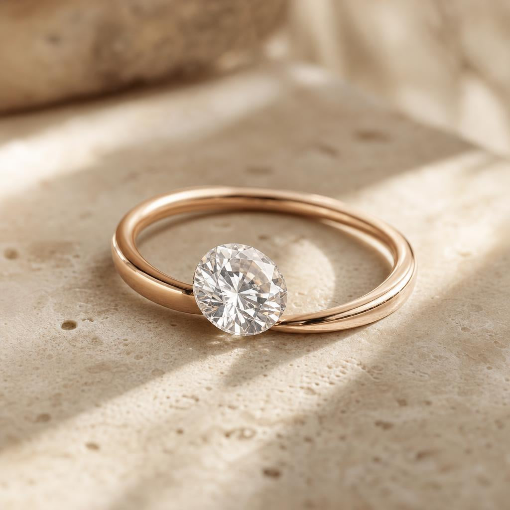 Clear faceted gemstone beside a blush rose gold band on cream stone