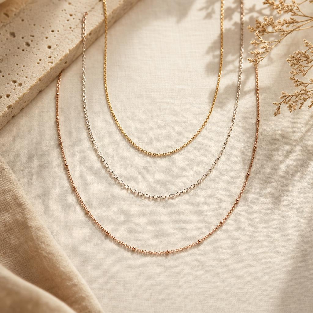 Three necklace chains of different lengths arranged in graduating arcs on linen