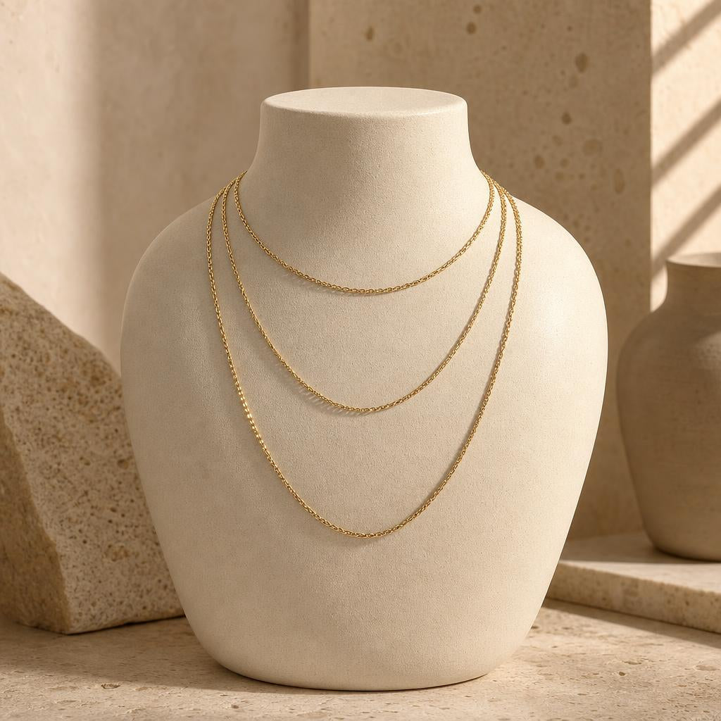 Three graduated necklace chains draped over a cream ceramic bust