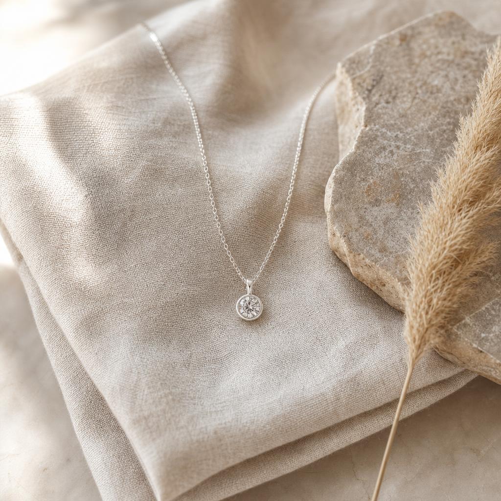 Silver pendant necklace with clear stone on oatmeal linen beside greige stone