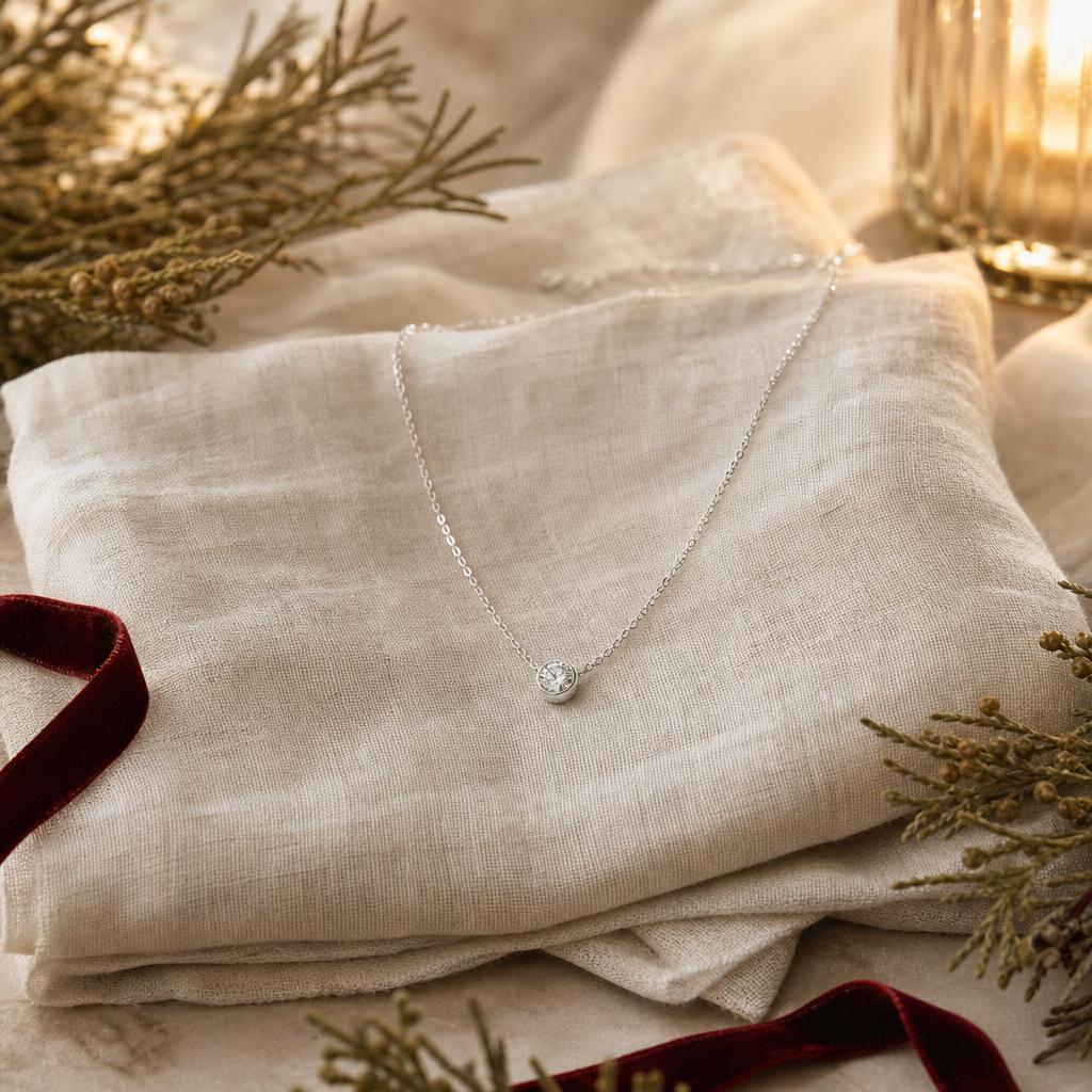 Silver solitaire pendant necklace on cream linen with evergreen and red ribbon