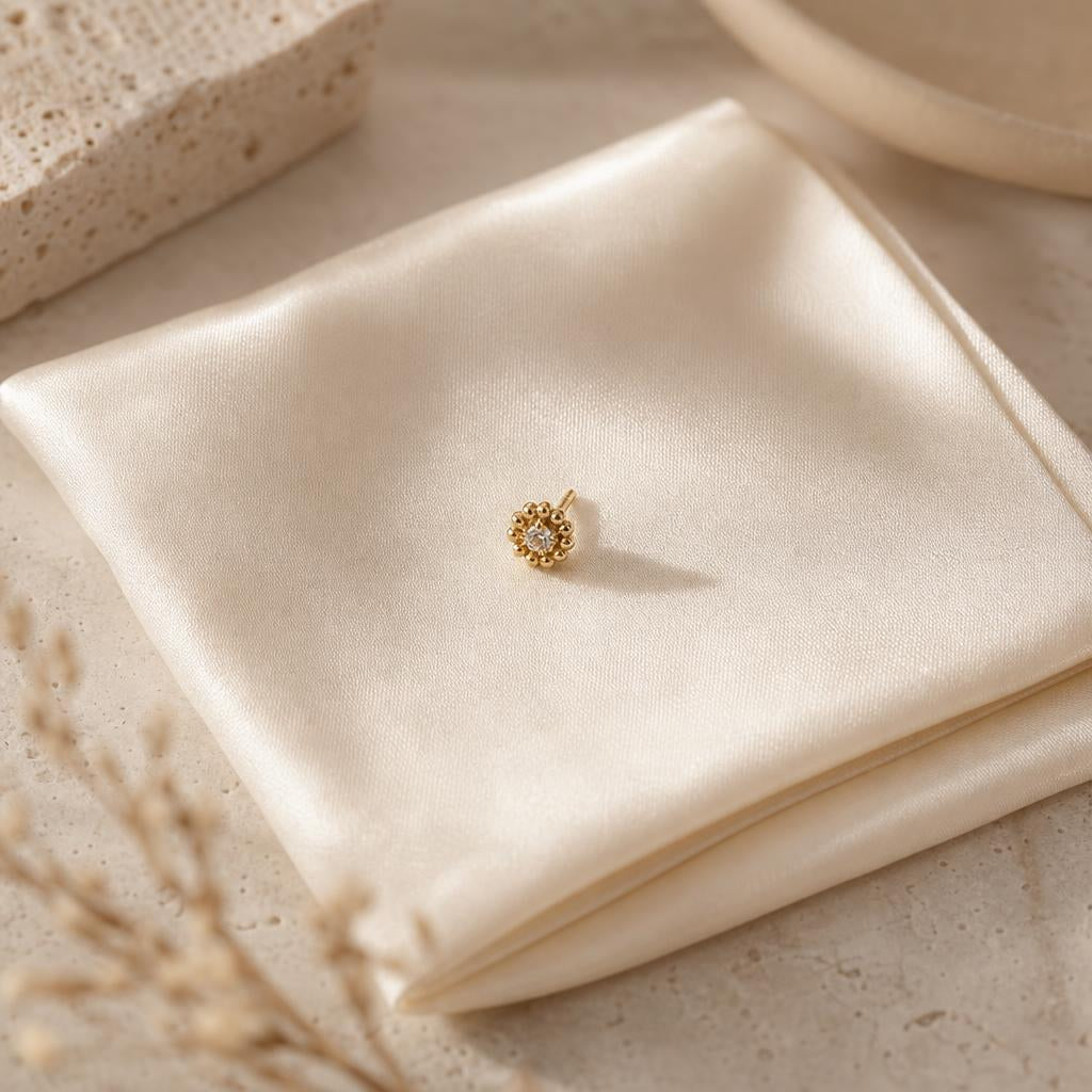 Single gold stud earring on folded cream silk with soft warm light