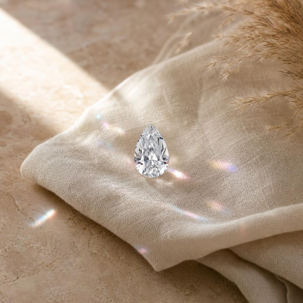 Pear shaped faceted gemstone on cream linen with soft prismatic light