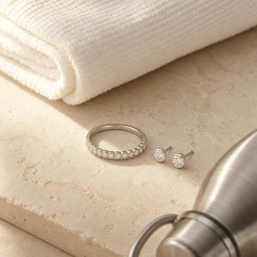 Bezel-set ring and stud earrings beside folded gym towel on stone surface