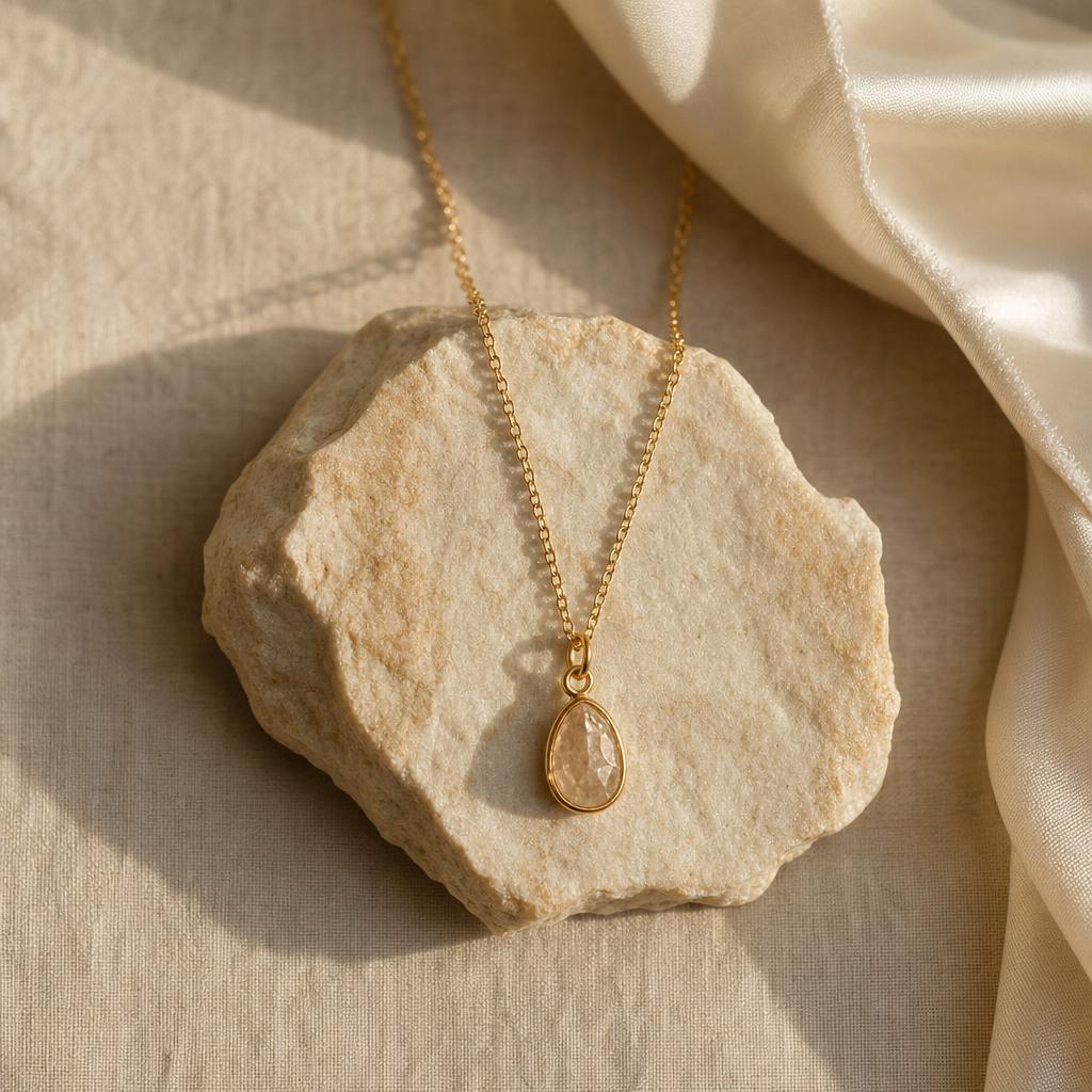 Delicate gold pendant necklace draped over warm cream stone and linen