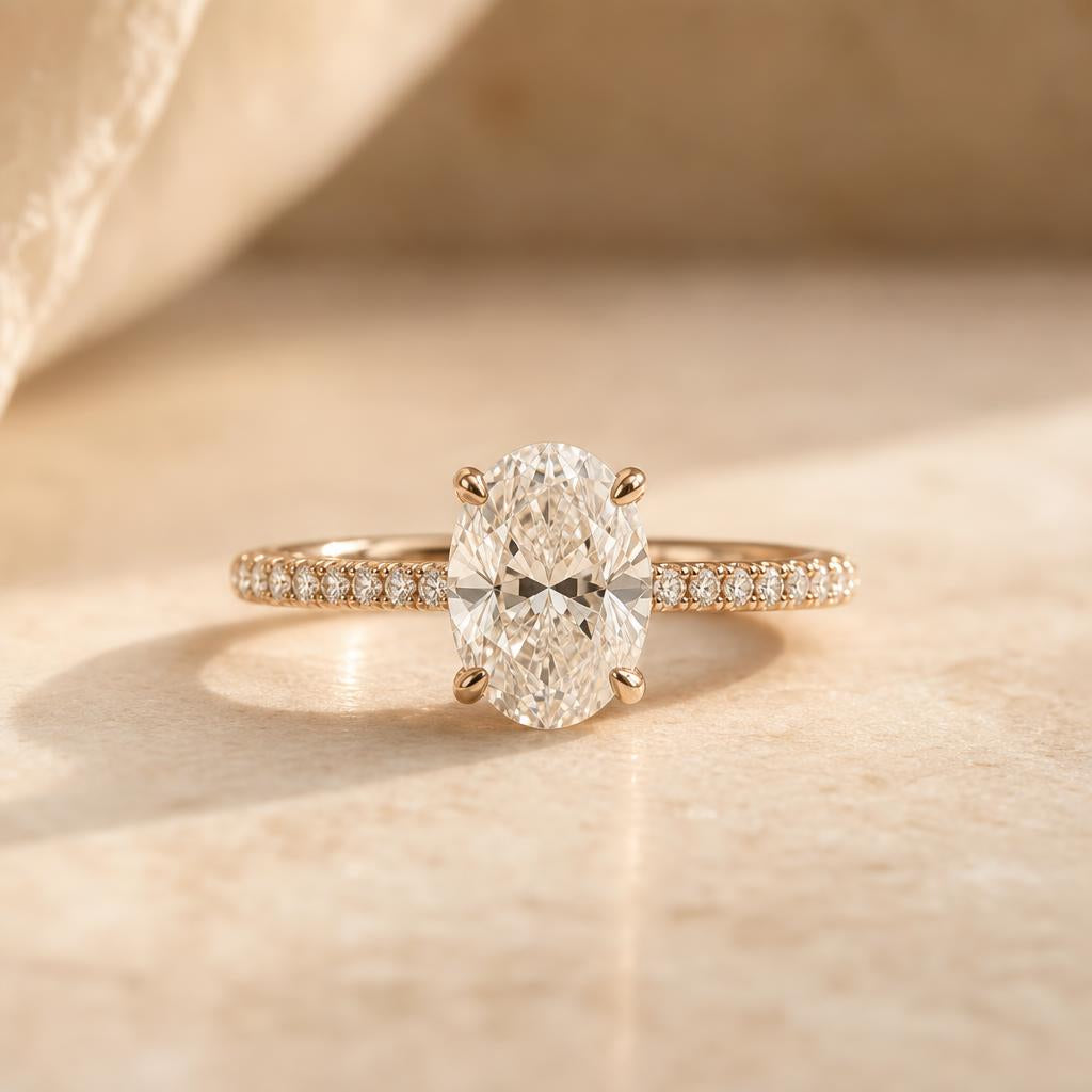 Oval-cut engagement ring with pavé band on warm cream stone background