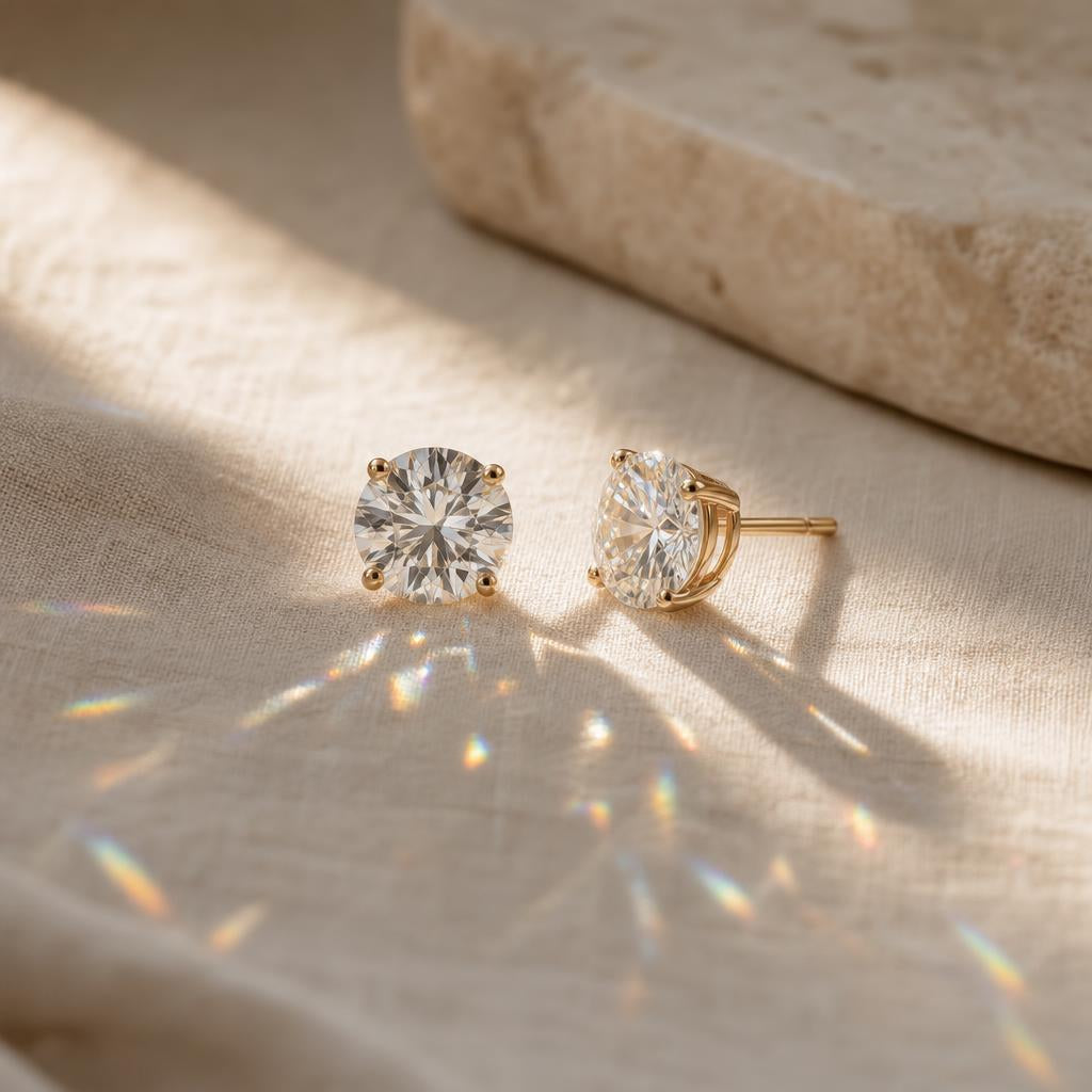 Pair of round moissanite stud earrings catching warm light on cream linen